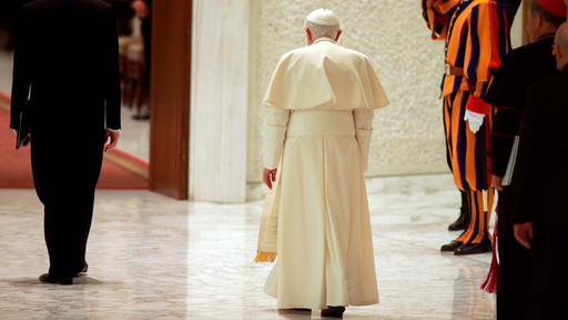 Papst Benedikt XVI. ist mit dem Rücken zur Kamera gewandt, er verlässt einen großen Raum.