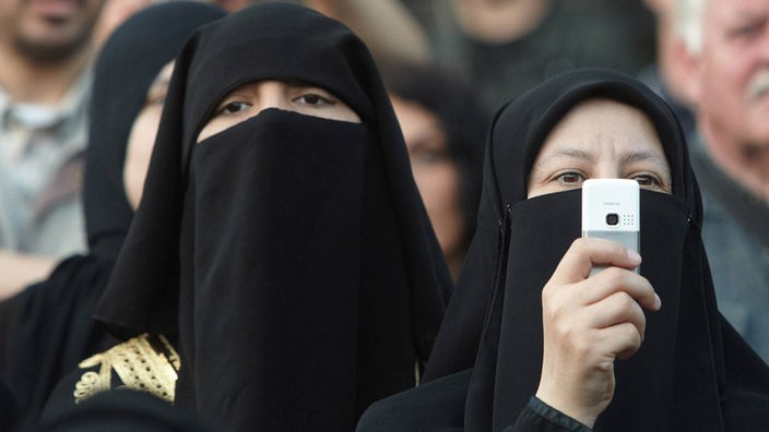 Schwarz Verschleierte Frauen, Nahaufnahme, eine hält ein weißes Handy in der Hand.