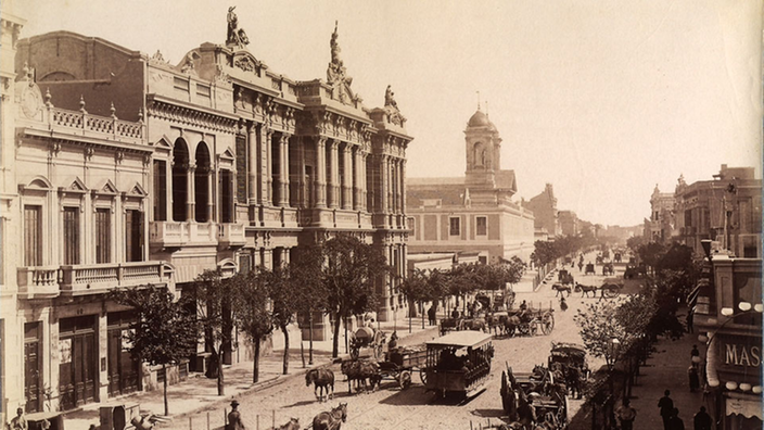 Schwarzweiß-Foto einer Straßenszene mit Prachthäusern und einer Straße mit einigen Pferdekutschen. | Bildquelle: Interfoto Schwarzweiß-Foto einer Straßenszene mit Prachthäusern und einer Straße mit einigen Pferdekutschen.