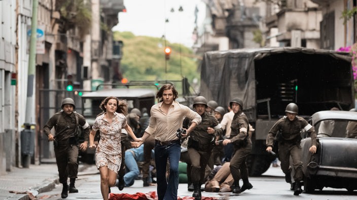 Filmszene: Ein Mann und eine Frau rennen vor Soldaten weg