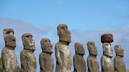 Acht Steinfiguren unterschiedlicher Höhe stehen nebeneinander.
