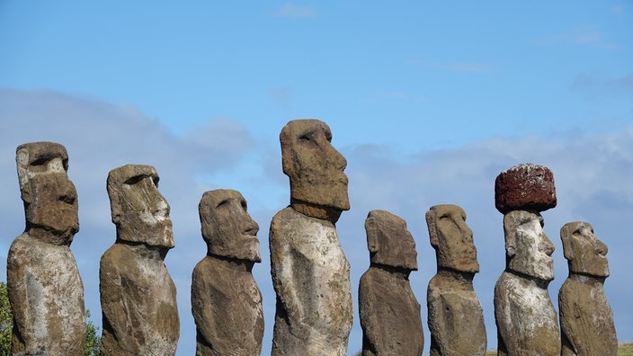 Acht Steinfiguren unterschiedlicher Höhe stehen nebeneinander.