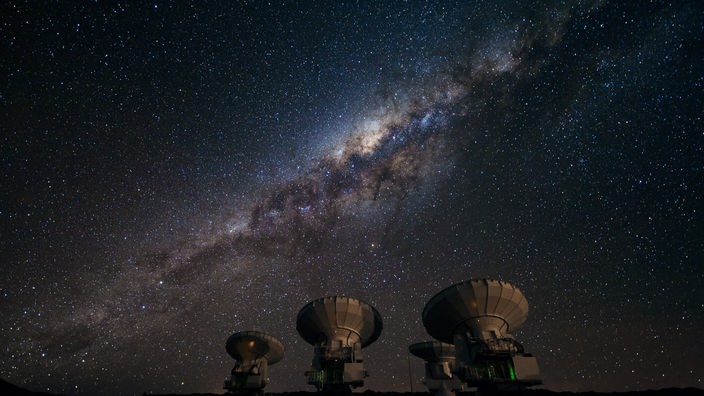 Verschiedene Radioteleskope zeigen auf den Sternenhimmel bei Nacht.