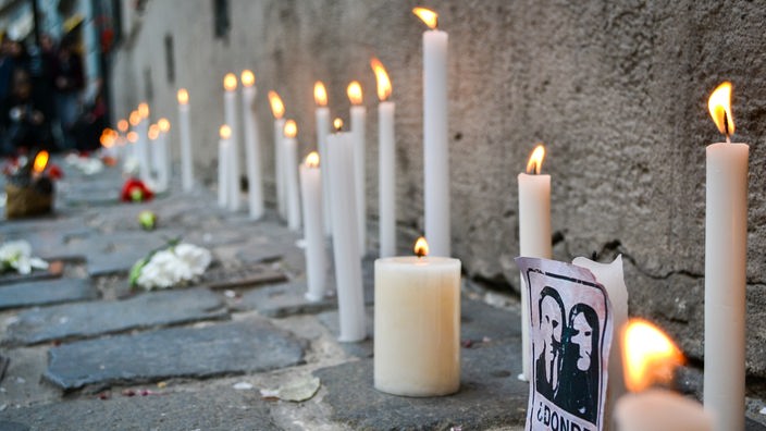 Kerzen und Karten mit der Aufschrift "¿Dónde están?" ("Wo sind sie?") stehen auf dem Boden.