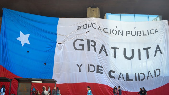 Eine große Flagge Chiles hängt an einem Gebäude mit der Aufschrift "Educación gratuita y de calidad" ("Bildung – gratis und von guter Qualität").