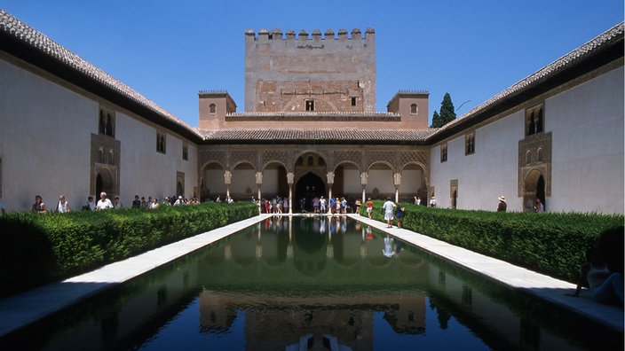 Innenhof in der Alhambra von Granada. Ein Turm und die Bögen des Innenhofes spiegeln sich in einem länglichen Wasserbecken. | Bildquelle: dpa/Roberto Vignoli Innenhof in der Alhambra von Granada. Ein Turm und die Bögen des Innenhofes spiegeln sich in einem länglichen Wasserbecken.