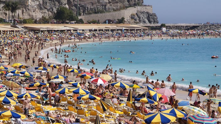 Überfüllter Strand mit blau-gelben Sonnenschirmen.