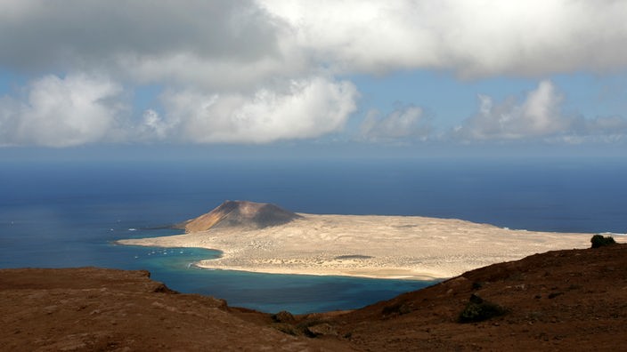 Blick auf eine vorgelagerte Insel mit hellem Sand und einem Vulkan.