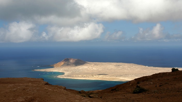 Blick auf eine vorgelagerte Insel mit hellem Sand und einem Vulkan. | Bildquelle: dpa Blick auf eine vorgelagerte Insel mit hellem Sand und einem Vulkan.