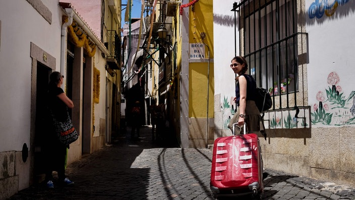 Frau mit Koffer in einer Gasse in Lissabon | Bildquelle: AFP/Patricia de Melo Moreira Frau mit Koffer in einer Gasse in Lissabon