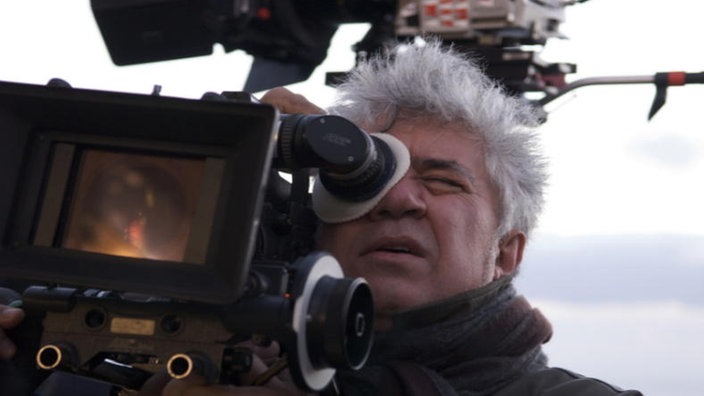 Almodóvar mit ergrautem Haar am Filmset von "Zerrissene Umarmungen" (2009), er blickt durch eine Kamera. | Bildquelle: Interfoto Almodóvar mit ergrautem Haar am Filmset von "Zerrissene Umarmungen" (2009), er blickt durch eine Kamera.