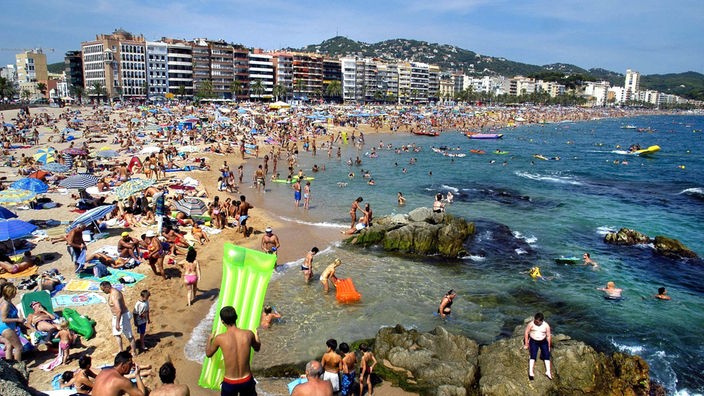 Massenhaft Touristen an einem Strand. Direkt hinter dem Strand reihen sich große Hotelbauten aneinander.