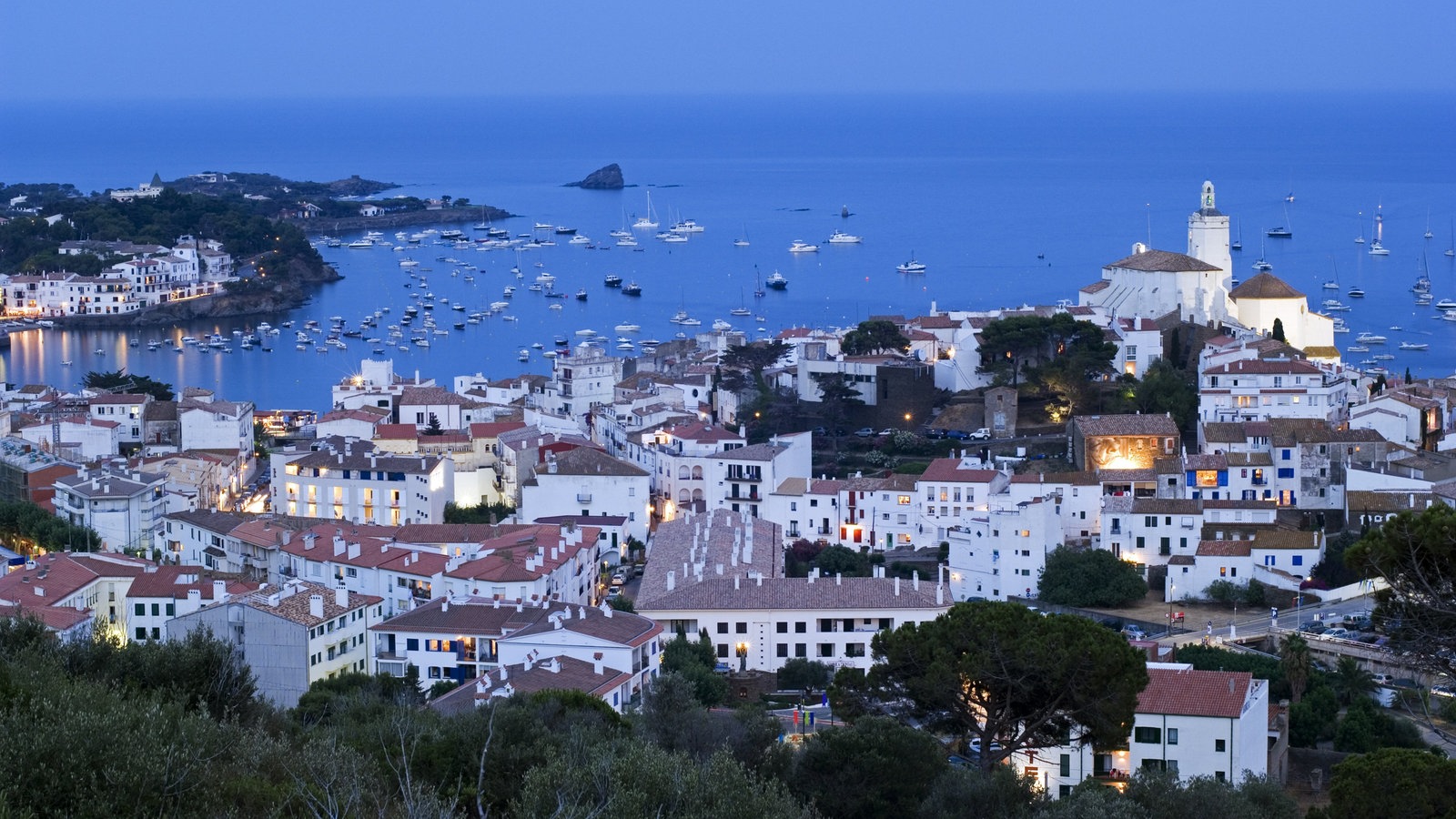 Blick von oben auf die weißen Häuser von Cadaques vor abendlichem Himmel