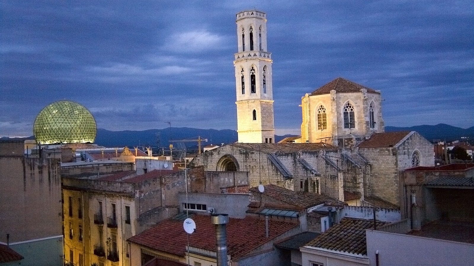 Blick über Dächer auf die abendlich angestrahlte Kirche von Figueres