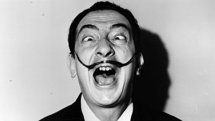Schwarzweiß-Porträt von Salvador Dalí mit gezwirbeltem Schnurrbart und verdrehten Augen.