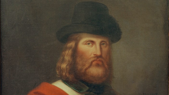 Schwarzweiß-Porträt des bärtigen Garibaldi mit einem gestreiften Umhang um die Schultern und einer verzierten Kappe auf dem Kopf.