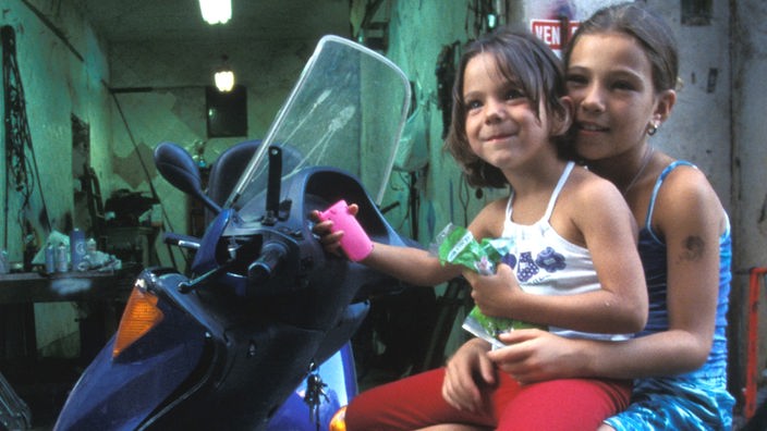 Zwei kleine Mädchen sitzen auf einer Vespa in einem heruntergekommenen Hinterhof von Palermo.