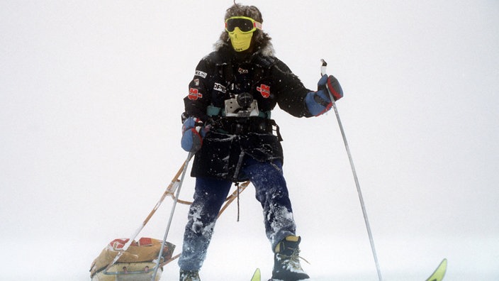 Das Foto zeigt Reinhold Messner dick vermummt mit Schutzmaske, Skibrille und Skianzug im Schnee. Er geht auf Skiern und zieht einen kleinen Lastenschlitten hinter sich her. | Bildquelle: dpa Das Foto zeigt Reinhold Messner dick vermummt mit Schutzmaske, Skibrille und Skianzug im Schnee. Er geht auf Skiern und zieht einen kleinen Lastenschlitten hinter sich her.