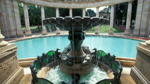 Springbrunnen vor Thermalbecken in alter, halboffener Thermenhalle mit Säulen.