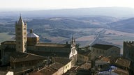 Blick über die Häuserdächer und den Kirchturm von Massa Marittima auf die sanft abfallenden Hügel der Umgebung