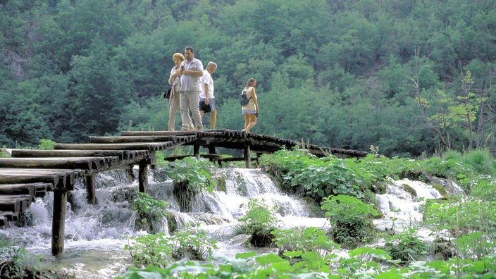 Touristen gehen über einen Steg, der über einen kleinen Wasserfall führt