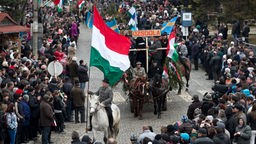 Auf einer Straßenparade hält ein Reiter eine große ungarische Flagge.