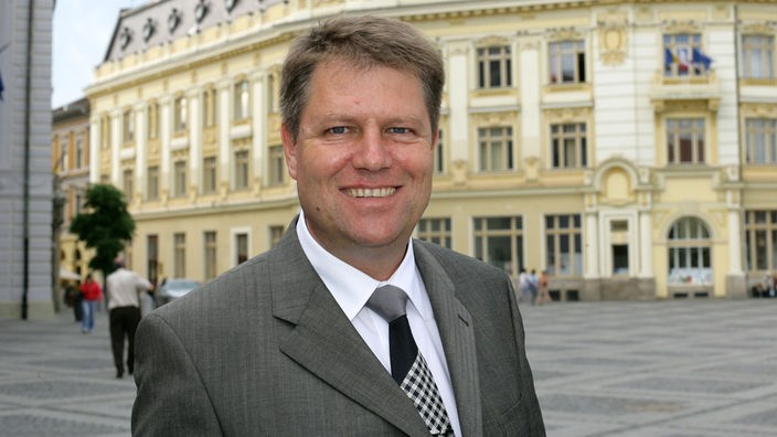 Der Oberbürgermeister von Sibiu/Hermannstadt Klaus Johannis steht lächelnd auf einem Platz.