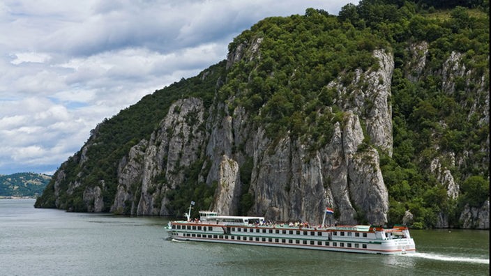 Ein Passagierschiff fährt auf der Donau entlang einer Felswand.