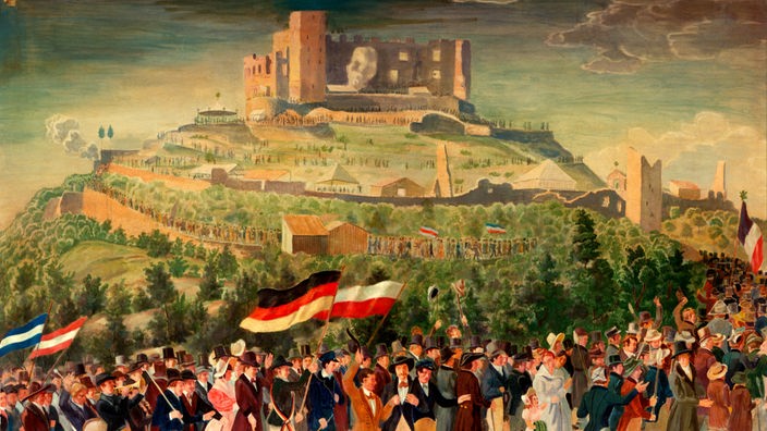 Eine zeitgenössische kolorierte Zeichnung zeigt eine große Menschenmenge, zum Teil mit schwarz-rot-goldenen Fahnen. Die Menge zieht auf einen Hügel, auf dem man das Hambacher Schloss erkennt.