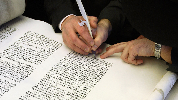 Auf dem Foto ist eine Hand zu sehen, die mit einer Feder in eine Thorarolle schreibt. | Bildquelle: dpa Picture-Alliance/Miguel Villagran Auf dem Foto ist eine Hand zu sehen, die mit einer Feder in eine Thorarolle schreibt.