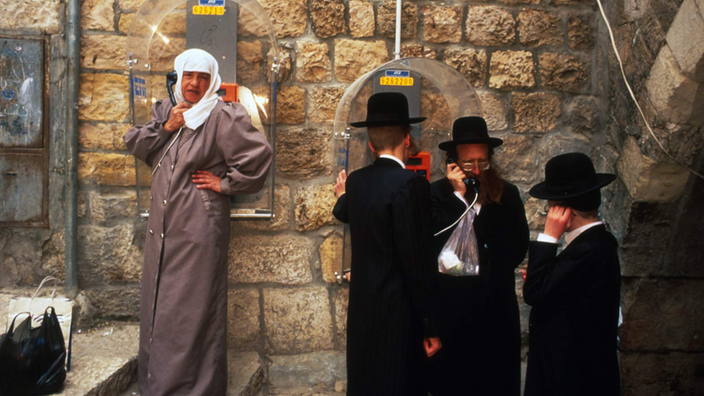 Ein Moslem und drei orthodoxe Juden, die öffentliche Telefone benutzen.