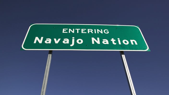 Straßenschild mit der Aufschrift 'Entering Navajo Nation' vor strahlend blauem Himmel.