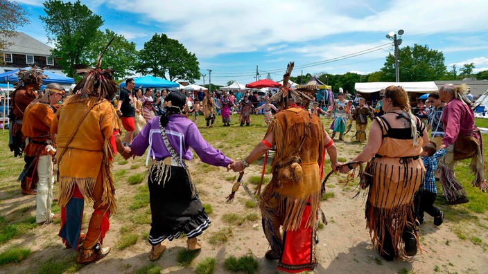 Mehrere festlich geschmückte Indianer tanzen in einem Kreis