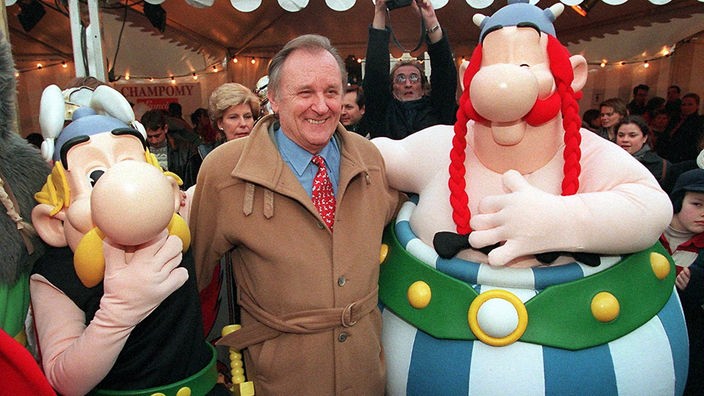 In der Mitte des Bildes steht ein älterer Herr, Asterix-Zeichner Albert Uderzo. Neben ihm stehen zwei als Asterix und Obelix verkleidete Menschen.