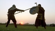 Zwei Männer stellen bei Sonnenuntergang einen Wikingerkampf nach