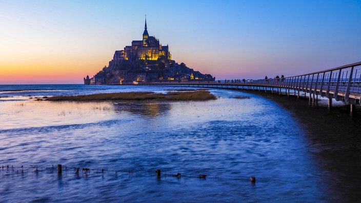 Pferd mit Kutsche und Besucher mit Hund auf einer Brücke vor dem Mont St. Michel