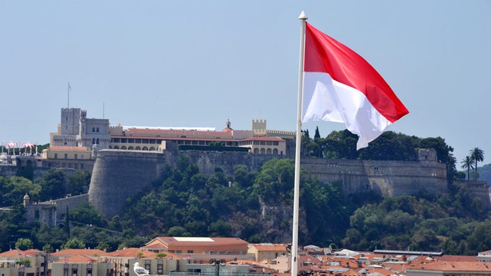 Die monegassische Flagge. Im Hintergrund der Palast der Grimaldis.