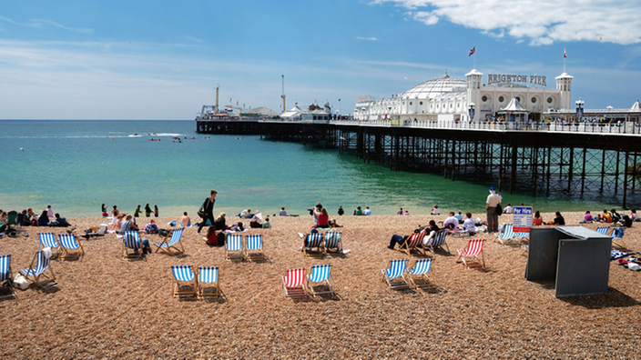 Strand von Brighton mit einem Pier, der ins Wasser führt, und Hochhäusern hinter der Strandpromenade.