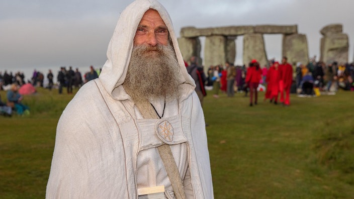 Ein heutiger Druide steht in weißer Kutte vor Stonehenge | Bildquelle: mauritius images / David Betteridge / Alamy / Alamy Stock Photos Ein heutiger Druide steht in weißer Kutte vor Stonehenge