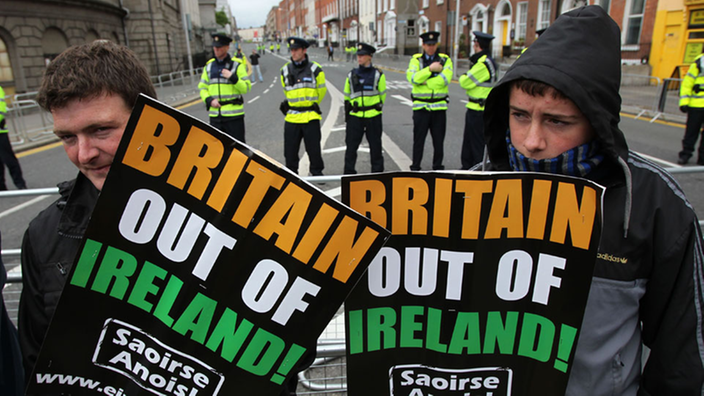 Zwei Iren halten jeweils ein Protestschild hoch, auf dem "Britain out of Ireland!" zu lesen ist.
