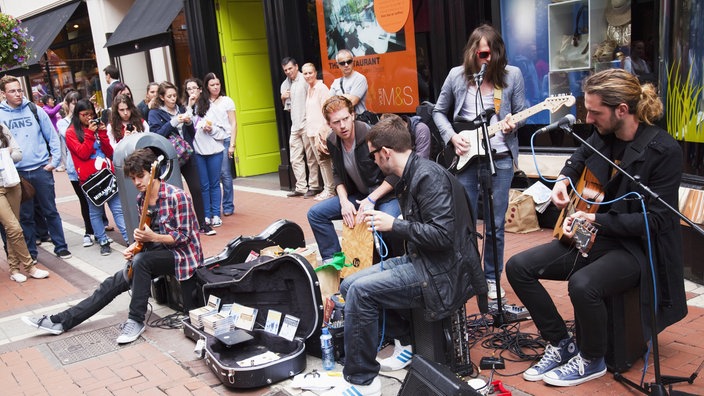 Eine junge Band sitzt auf der Straße und spielt auf ihren Instrumenten | Bildquelle: picture alliance / Design Pics Eine junge Band sitzt auf der Straße und spielt auf ihren Instrumenten