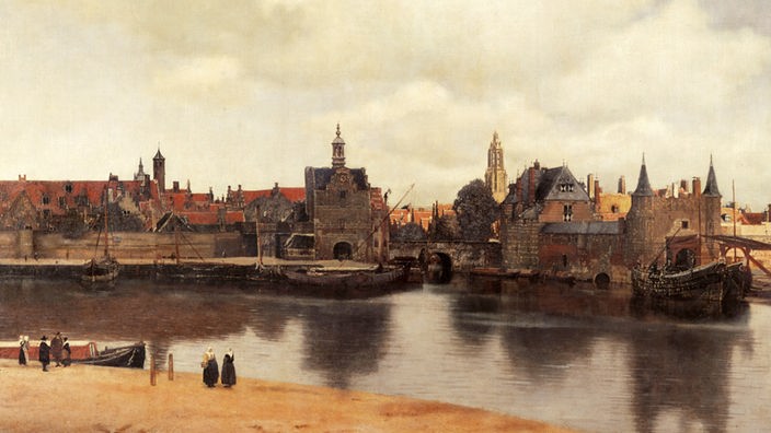 Das Gemälde zeigt eine Stadt an einem Fluss: Häuser, zum Teil mit Türmen, eine Kirche, Boote, die am Ufer liegen.