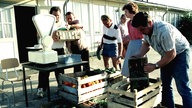Meherer Menschen stehen um eine Waage zwischen Kisten mit Gemüse. (1983)