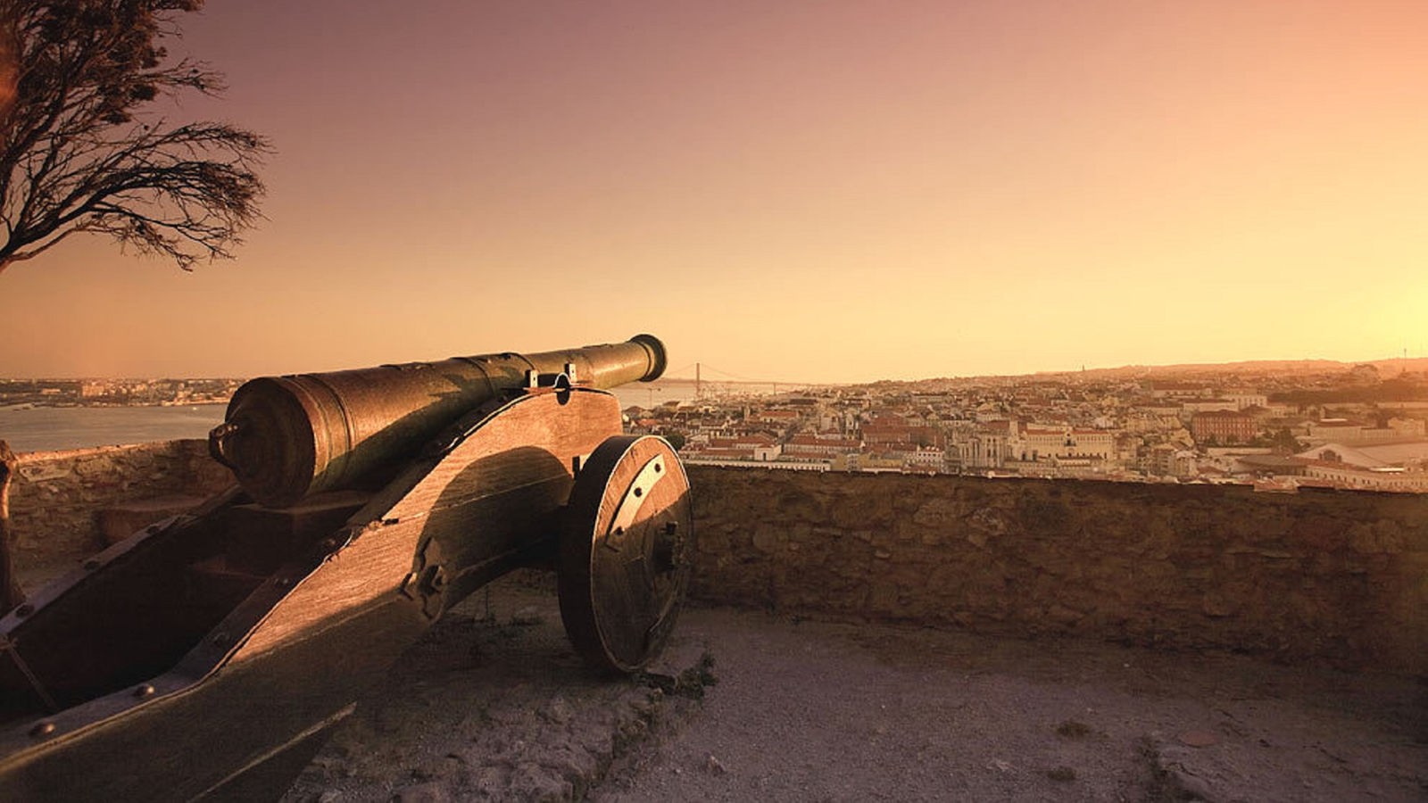Burg Castelo de São Jorge mit einem Kanonenrohr bei Sonnenuntergang und Blick übr die Stadt.