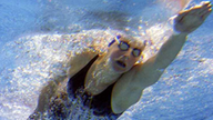 Unterwasseraufnahme einer Leistungsschwimmerin in schwarzem Badeanzug beim Kraulen