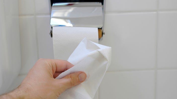 Nahaufnahme einer Toilettenrolle und einer Hand, die Papier