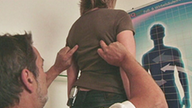 Ein Podoätiologe untersucht tastet mit seinen Fingern zwischen den Schulterblätter einer Frau.