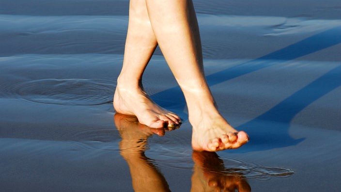 Füße gehen durch flaches Wasser am Strand.