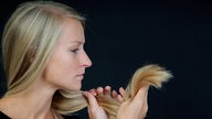 Blonde Frau betrachtet ihre Haarspitzen