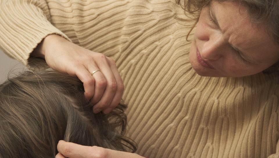 Eine Mutter sucht die Haare ihrer Tochter nach Läusen ab.